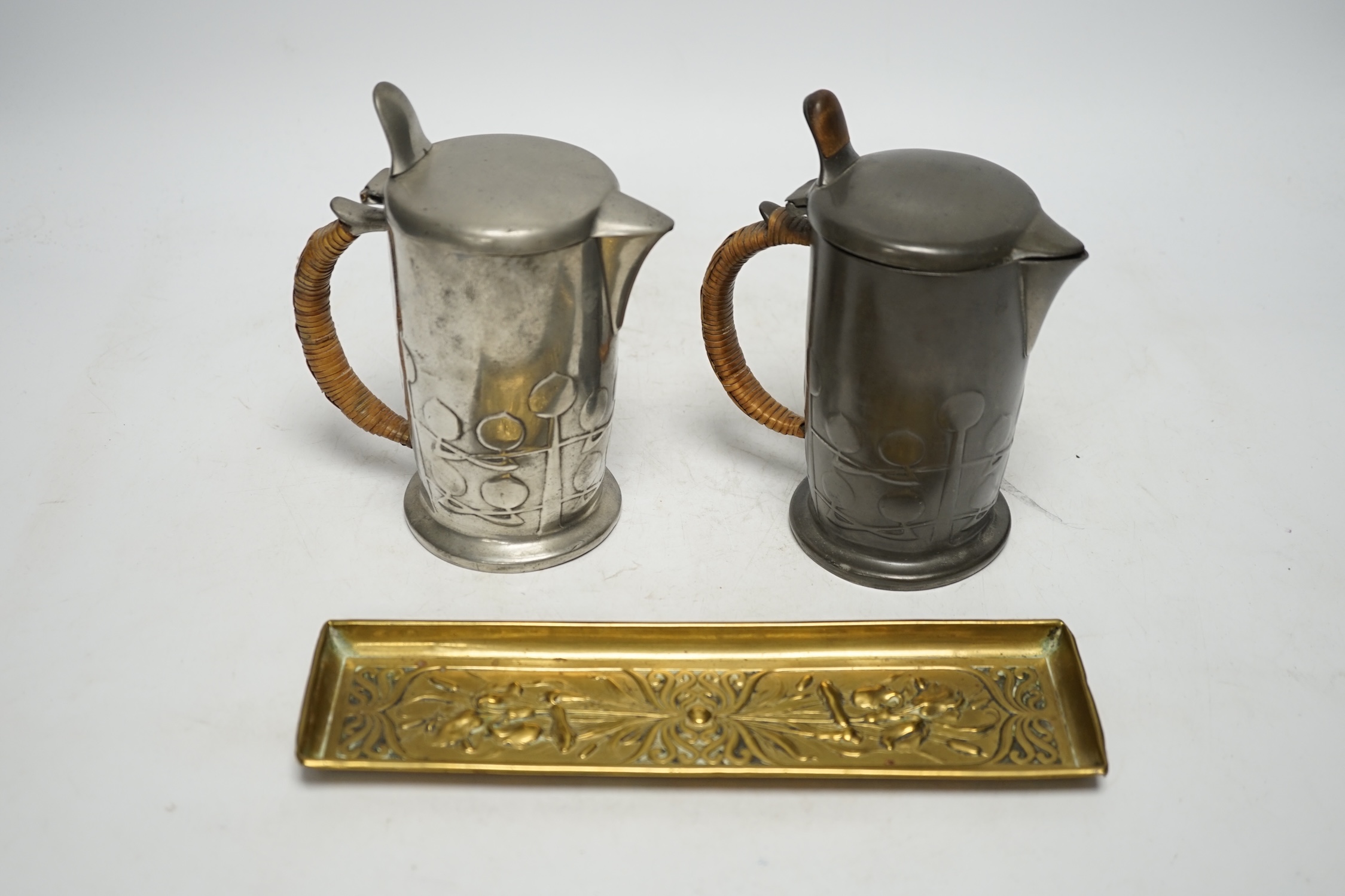 Archibald Knox (1864-1933) for Liberty & Co, two Tudric hot water jugs and an Art Nouveau brass pen tray, tray 24cm long (3). Condition - fair to good